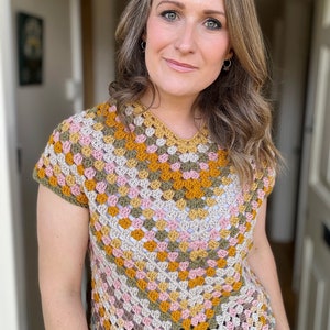May include: A crocheted top with a geometric pattern in shades of brown, pink, and yellow. The top has short sleeves and a scoop neck.
