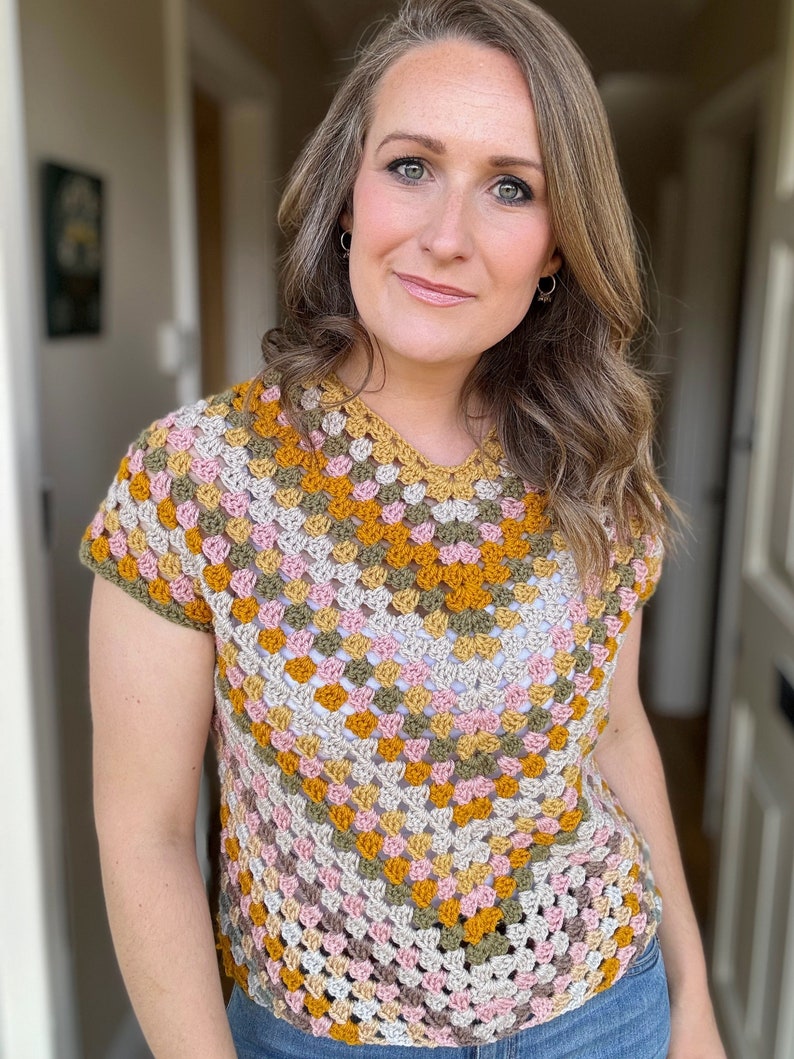 May include: A crocheted top with a geometric pattern in shades of brown, pink, and yellow. The top has short sleeves and a scoop neck.