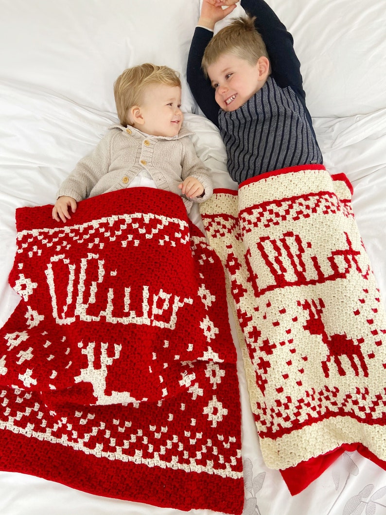 Puede incluir: Dos ni&ntilde;os est&aacute;n tumbados en una cama blanca con sus cabezas en los extremos opuestos de la cama. Cada ni&ntilde;o est&aacute; debajo de una manta de ganchillo con un dise&ntilde;o diferente. La manta de la izquierda es roja con copos de nieve blancos y la palabra "Oliver" en blanco. La manta de la derecha es blanca con copos de nieve rojos y la palabra "Lola" en rojo.