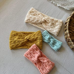 May include: Four knitted headbands in various colors: cream, mustard yellow, light blue, and coral pink. Each headband features a twisted knot design. The headbands are made of a textured knit fabric, perfect for adding a touch of style.