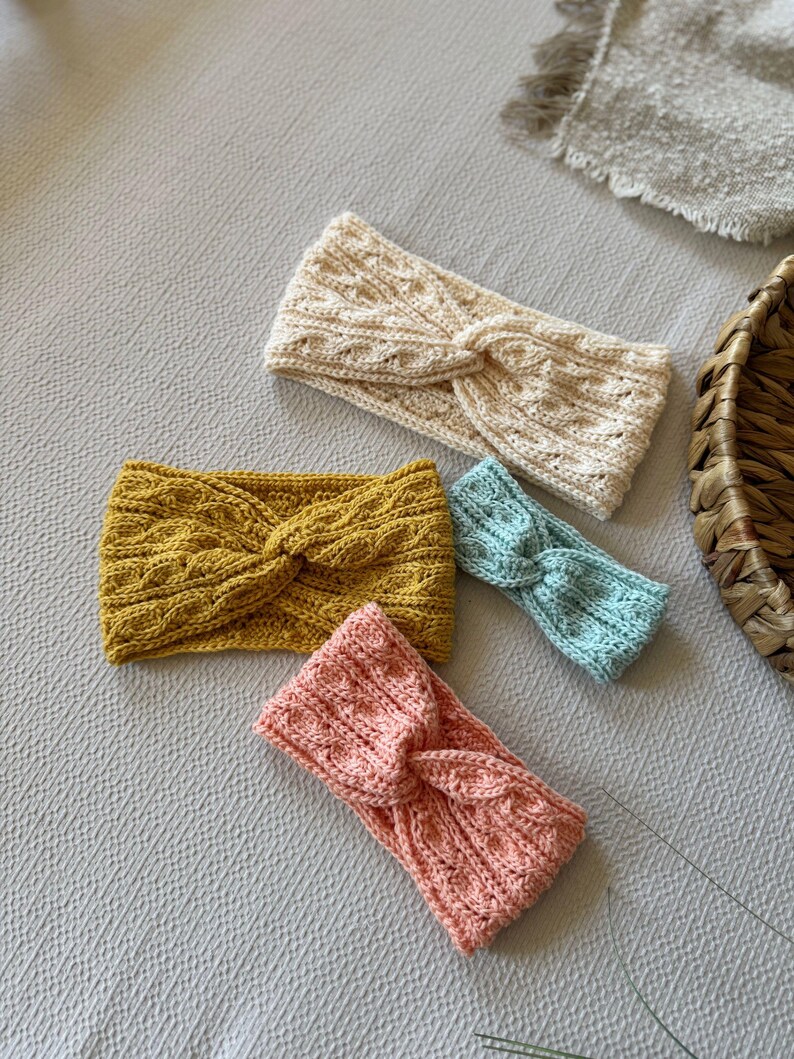 May include: Four knitted headbands in various colors: cream, mustard yellow, light blue, and coral pink. Each headband features a twisted knot design. The headbands are made of a textured knit fabric, perfect for adding a touch of style.
