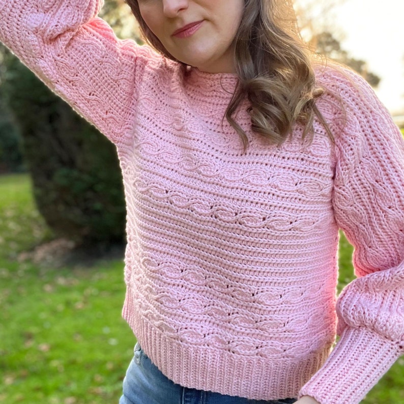 Woman holding hair back wearing pink crop crochet sweater pattern.