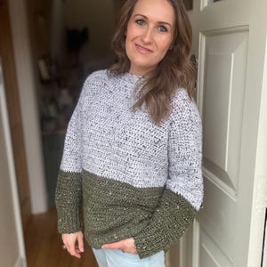 Puede incluir: Un su&eacute;ter de crochet de dos tonos con la parte superior gris claro y la inferior verde oscuro. El su&eacute;ter tiene un cuello redondo y mangas largas.