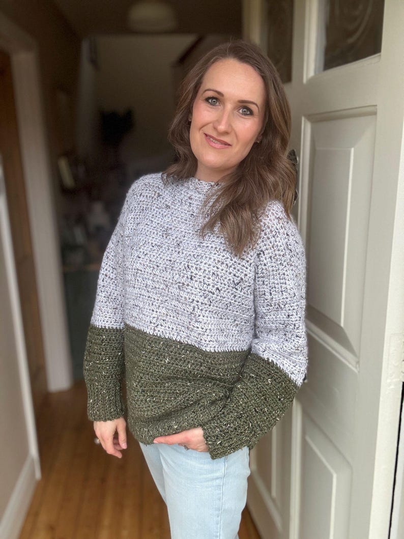 Puede incluir: Un su&eacute;ter de crochet de dos tonos con la parte superior gris claro y la inferior verde oscuro. El su&eacute;ter tiene un cuello redondo y mangas largas.