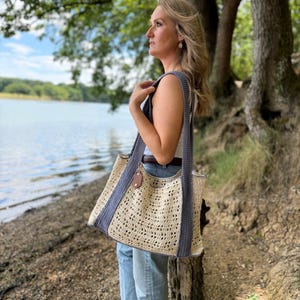 Puede incluir: Un bolso tote rectangular de ganchillo con un cuerpo calado de color crema y patr&oacute;n texturizado. El bolso incluye dos correas anchas de hombro de color gris oscuro y un borde gris oscuro, acentuado por una peque&ntilde;a etiqueta de cuero marr&oacute;n.