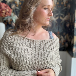 May include: A beige off-the-shoulder crochet sweater with long sleeves.