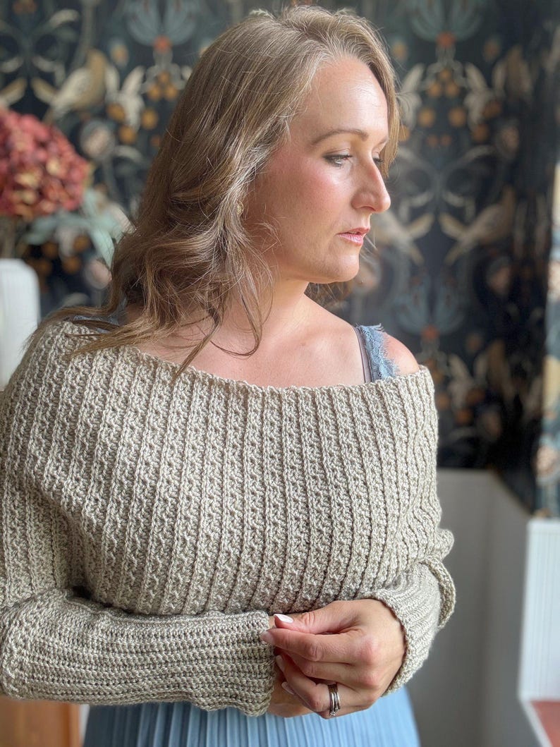 May include: A beige off-the-shoulder crochet sweater with long sleeves.