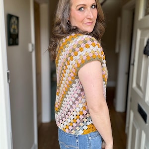 May include: A crocheted top with a granny square pattern in shades of pink, green, beige, and mustard yellow. The top has short sleeves and a scoop neck.