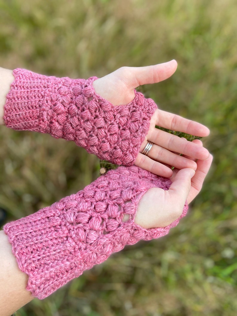 May include: A pair of pink crocheted fingerless gloves with a textured design. The gloves have a hole for the thumb.