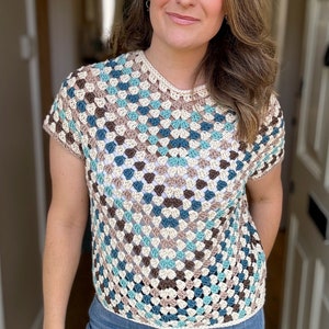 May include: A crocheted top with a geometric pattern in shades of brown, blue, and white. The top has short sleeves and a round neckline.