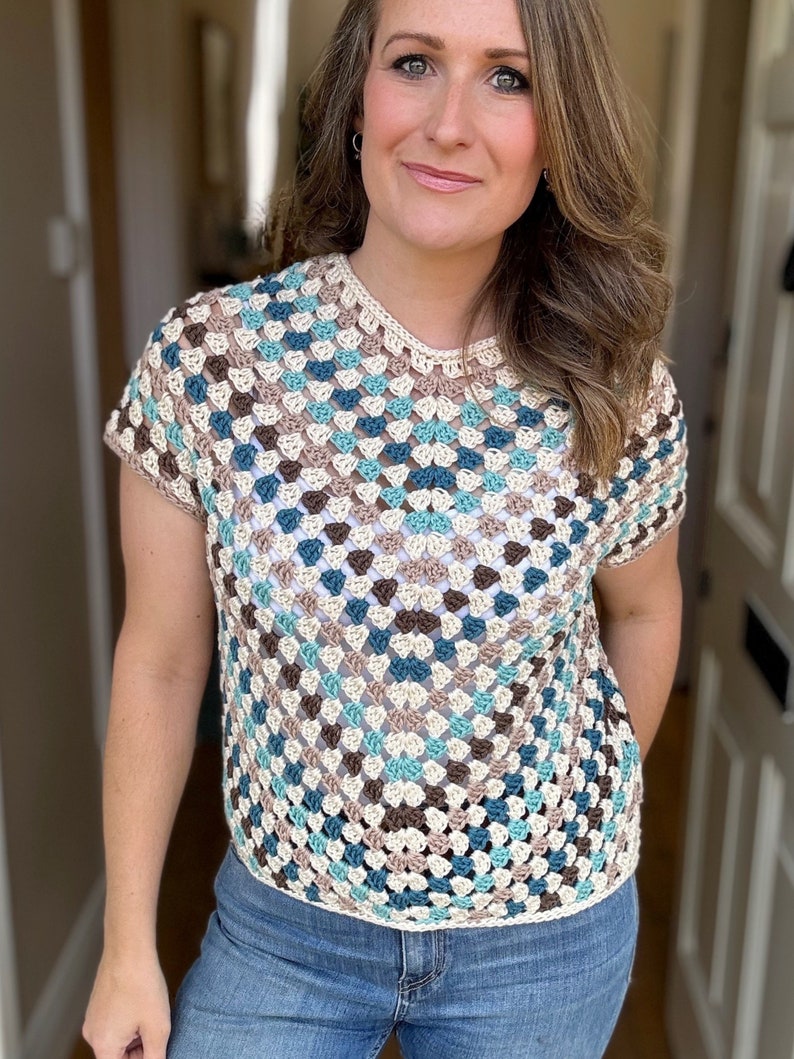 May include: A crocheted top with a geometric pattern in shades of brown, blue, and white. The top has short sleeves and a round neckline.