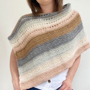 May include: A crocheted poncho with a striped pattern in shades of pink, brown, gray, and white. The poncho has a wide, open neckline and a loose, flowing fit.