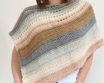 May include: A crocheted poncho with a striped pattern in shades of pink, brown, grey, and white. The poncho has a wide, open neckline and a loose, flowing fit.