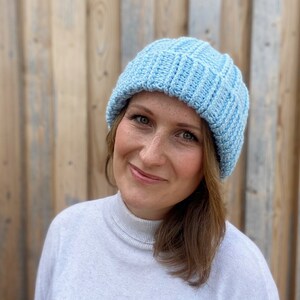 May include: A light blue knitted beanie hat with a ribbed texture. The hat is worn by a person with brown hair and is positioned on their head.