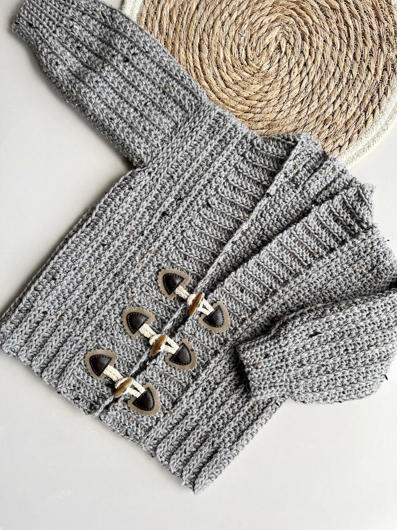 Pu&ograve; includere: Un cardigan di maglia grigia con bottoni marroni. Il cardigan ha una trama a coste ed &egrave; realizzato con un filato maculato.