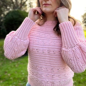 Woman wearing cropped crochet sweater with arms up to tuck hair behind.