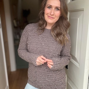 Puede incluir: Un su&eacute;ter de crochet marr&oacute;n con una textura brillante. El su&eacute;ter tiene mangas largas y un cuello redondo.