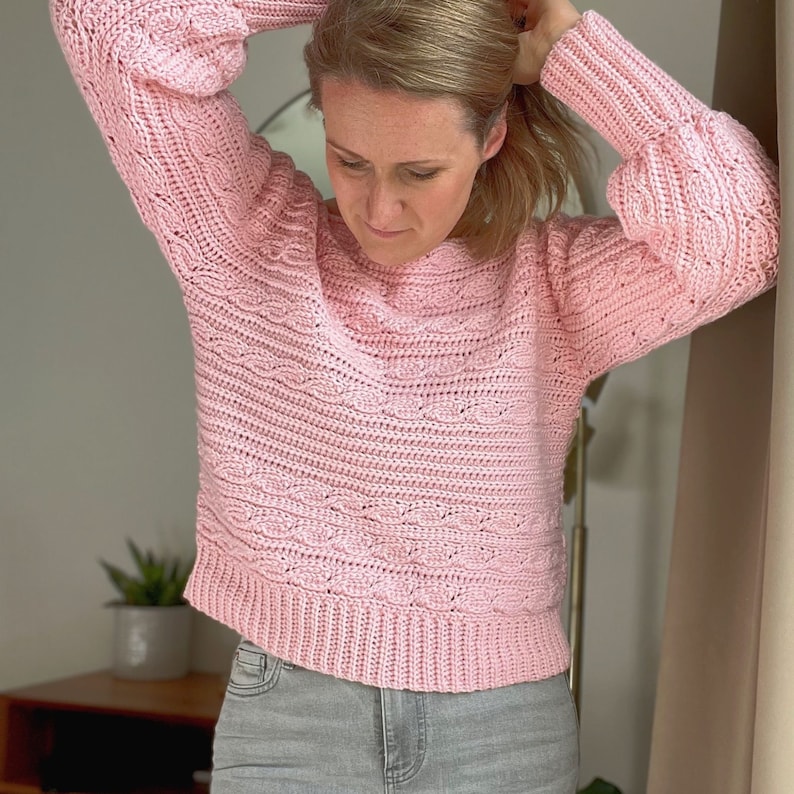 Woman holding hair up wearing crochet sweater with long rib cuffs and waist ribbing.