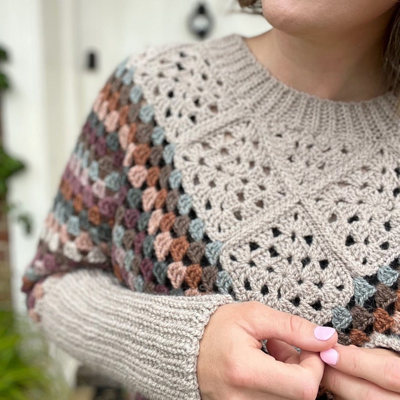 Puede incluir: Un su&eacute;ter de crochet beige con un patr&oacute;n geom&eacute;trico multicolor en los hombros y las mangas.