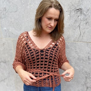 Puede incluir: Un top de crochet de color terracota con un lazo en la cintura. El top tiene un corte holgado y un escote en V.
