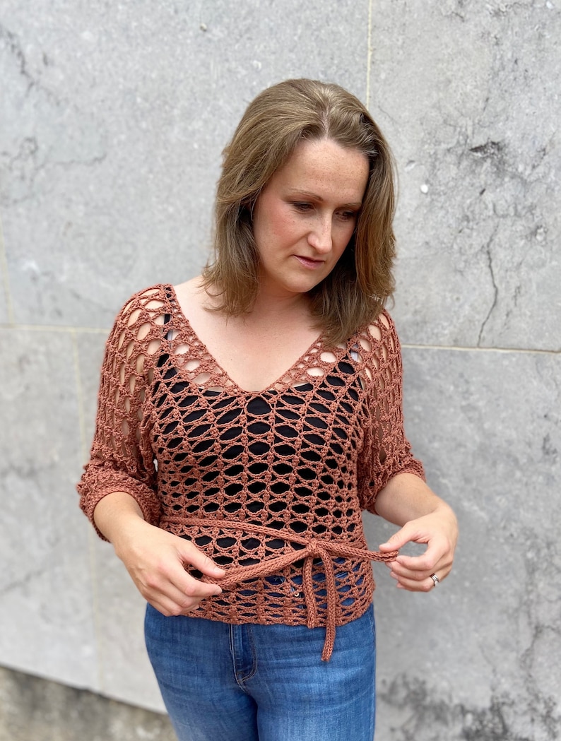 Puede incluir: Un top de crochet de color terracota con un lazo en la cintura. El top tiene un corte holgado y un escote en V.