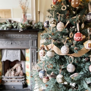 May include: A Christmas tree decorated with knitted ornaments in various colors and patterns, including red, white, brown, and green. The tree is decorated with pine cones and burlap ribbon.