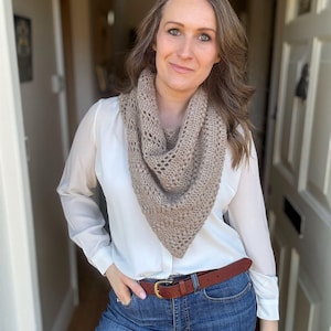 Op de afbeelding: Een vrouw draagt een wit blouse met een bruine gehaakte sjaal en blauwe jeans. Ze draagt een bruine leren riem met een gouden gesp.