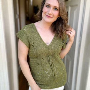 Puede incluir: Un top de crochet verde con cuello en V y mangas cortas. El top tiene un lazo en la cintura.