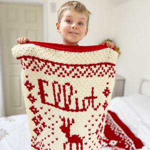 Child holding up a red and white personalised crochet christmas blanket.