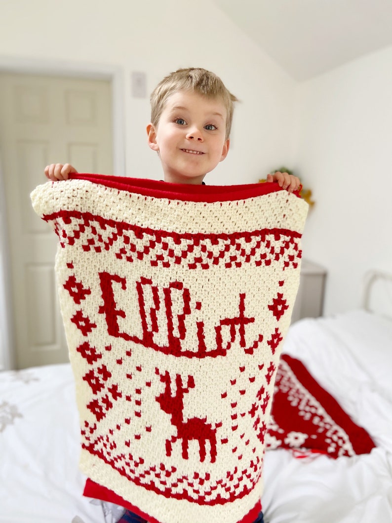 Child holding up a red and white personalised crochet christmas blanket.