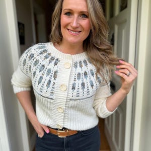 Puede incluir: Cárdigan color crema con botones y canesú estampado con detalles en azul y gris. El suéter tiene dobladillo y puños de canalé y se combina con vaqueros de lavado oscuro y un cinturón marrón.