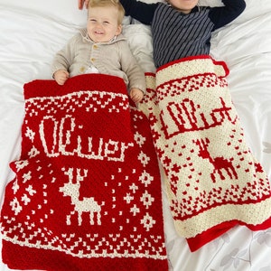 Two children each in a red and white crocheted christmas blankets. Each has a name and a reindeer on it.