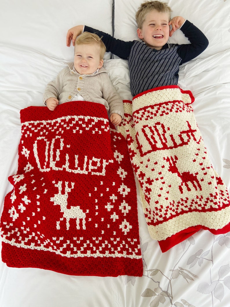 Two children each in a red and white crocheted christmas blankets. Each has a name and a reindeer on it.