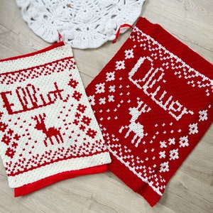 Two red and white crocheted christmas blankets. Each has a name and a reindeer on it.
