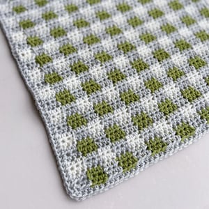 May include: A crocheted square with a checkered pattern in green and gray.