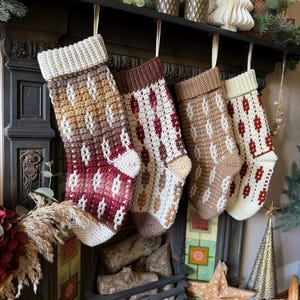 May include: Four handmade Christmas stockings with diamond patterns in shades of brown, cream, and red hang from a dark mantelpiece. Each stocking has a cream-coloured cuff and is suspended by a cream ribbon. A cosy, festive decoration.