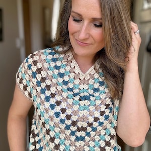 May include: A crocheted top with a geometric pattern in shades of brown, beige, teal, and blue. The top has a v-neck and short sleeves.