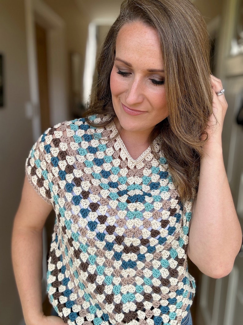 May include: A crocheted top with a geometric pattern in shades of brown, beige, teal, and blue. The top has a v-neck and short sleeves.