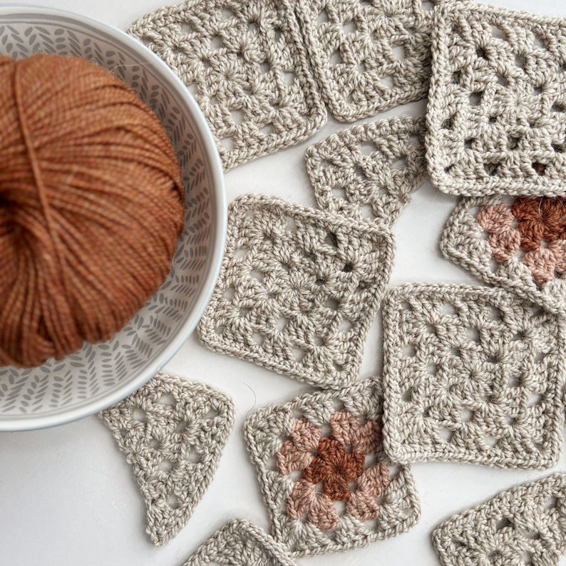 Puede incluir: Una colecci&oacute;n de cuadrados de ganchillo de color beige, algunos con un centro marr&oacute;n y rosa. Un bol de hilo marr&oacute;n est&aacute; en el fondo.
