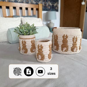 May include: Set of three cream-colored crochet baskets with brown bunny designs. The baskets vary in size and have a neutral color palette. The image also includes the text "3 sizes".