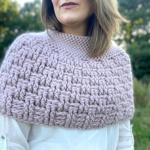 May include: A close-up of a light pink crocheted cowl or neck warmer. The cowl is made with a textured stitch pattern.