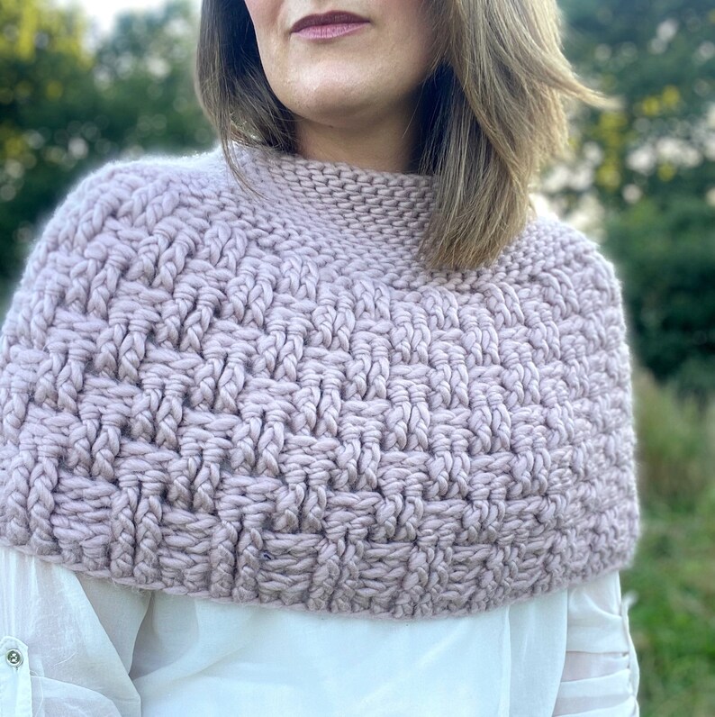 May include: A close-up of a light pink crocheted cowl or neck warmer. The cowl is made with a textured stitch pattern.