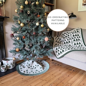 May include: A crochet Christmas tree skirt and matching throw blanket featuring a repeating dark green pine tree pattern on a cream background. The items have a dark green ribbed border. A circular sign reads CO-ORDINATING PATTERNS AVAILABLE.