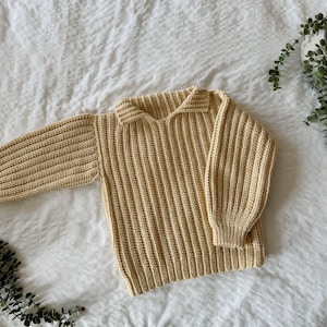 K&ouml;nnte beinhalten: Ein hellgelber Strickpullover mit Kragen. Der Pullover hat eine gerippte Struktur und lange &Auml;rmel.