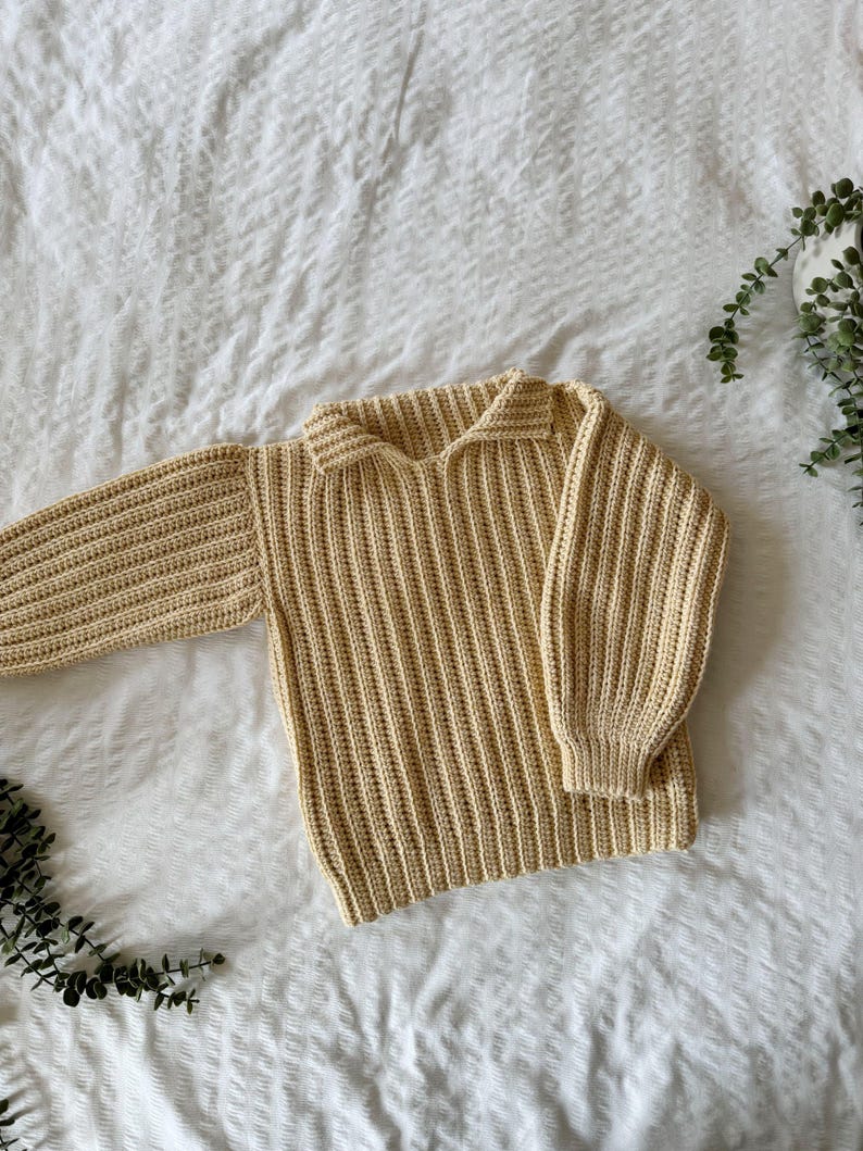 K&ouml;nnte beinhalten: Ein hellgelber Strickpullover mit Kragen. Der Pullover hat eine gerippte Struktur und lange &Auml;rmel.