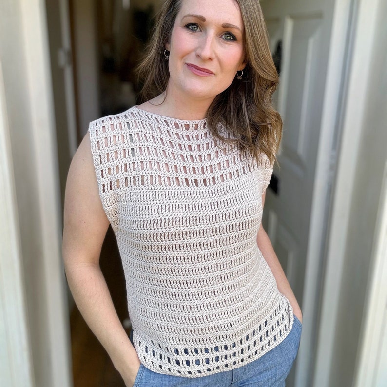 May include: A beige crochet top with a sleeveless design and a loose fit. The top has a delicate openwork pattern throughout.