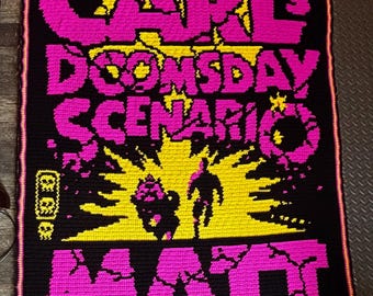 May include: A rectangular crochet blanket featuring a black background with bright pink and yellow text and graphics. The text reads CARL'S DOOMSDAY SCENARIO, MATT, and DINNIMAN. The design includes a yellow sunburst and two silhouettes.