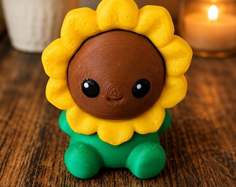 May include: A 3D printed figurine shaped like a sunflower with a brown center, bright yellow petals, and a green base. The center features two black eyes with white highlights. The surface has visible horizontal layer lines from the printing process.
