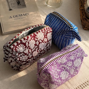 May include: Three quilted zipped pouches in different colours and patterns. One is deep red with a white floral print, one is light purple with a white floral print, and one is blue with white vertical stripes. Each has a gold-toned metal zip.