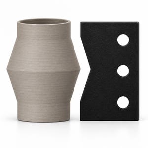 May include: A light gray, tapered cylindrical vase with a matte finish positioned next to a rectangular black tool featuring a notched side and three circular cutouts arranged in a vertical line, providing a contrast in shape and texture.